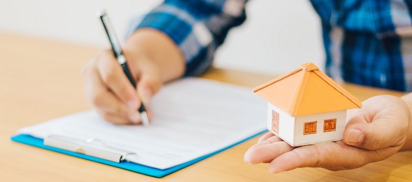 Un personne rédiger un document en tenant une maison miniature en papier